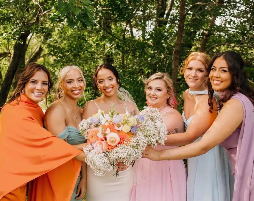 The bride and five bridesmaids outdoors, holding her bouquet together